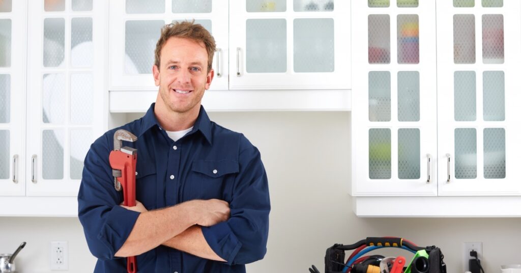 Plumber standing in kitchen, smiling, and holding a wrench.